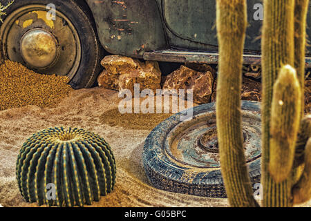 La carcassa di un vecchio arrugginito auto nel deserto di sabbia circondata da rocce e cactus Foto Stock