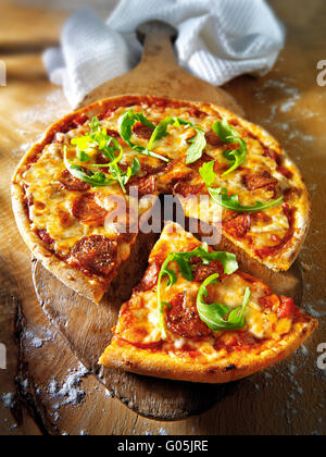 Cotto intero pomodoro e formaggio salsiccia per pizza pizza con rucola e una fetta tagliata Foto Stock