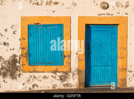 Vecchia facciata di una casa con giallo incorniciato di porta e finestra, sia di colore blu. Lampada sopra la porta. Foto Stock