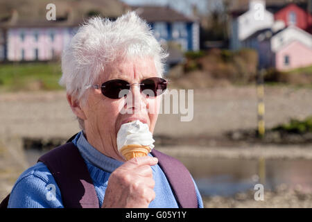 Autentica anziana anziana anziana anziana anziana anziana anziana persona pensionati con occhiali da sole scuri e mangiare un cono gelato in un giorno estivo. Aberaeron Galles Gran Bretagna Foto Stock