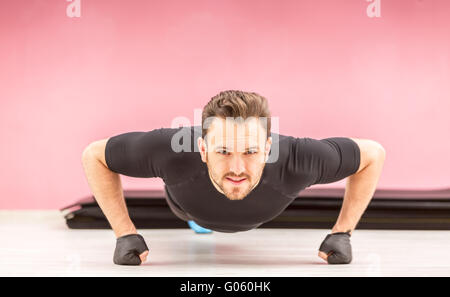 Ritratto di un giovane uomo bello fare pushups sui pugni in una palestra. Foto Stock