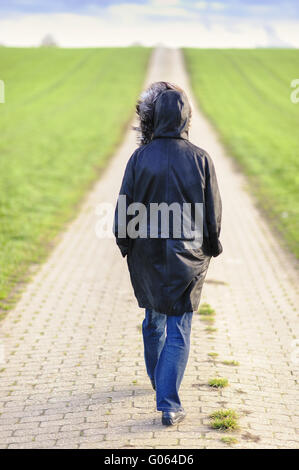 Una sola donna in vista posteriore va su una strada sterrata Foto Stock