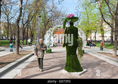 Russia, Mosca Festa di Primavera è in corso il 29 aprile 2016. Il festival è associato a un numero di vacanze Russo: la Pasqua ortodossa russa e lavoratore del giorno che vengono ad essere celebrata il 1 maggio e la Giornata della Vittoria, 9 maggio. Unidentified uomo passa dalla scultura di una donna vestita secondo la moda del XIX secolo. La scultura è fatta di erba artificiale e installato su Viale Tverskoi boulevard. Credito: Alex Immagini/Alamy Live News Foto Stock