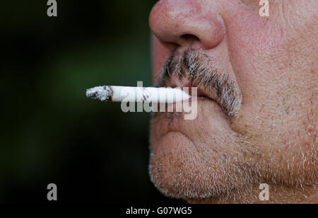 Fumare una sigaretta contro uno sfondo scuro Foto Stock