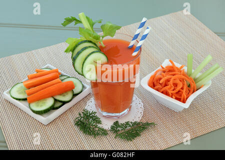 La carota e il sedano e il cetriolo health drink con verdure a fettine su una stuoia di bambù in legno su sfondo verde. Foto Stock