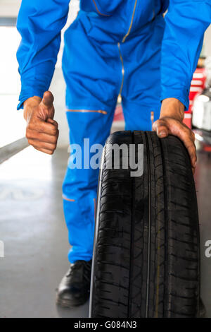 Mechanic tenendo un auto ruota con il pollice in alto segno in garage auto service Foto Stock