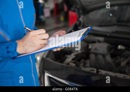 Giovane ingegnere meccanico tenendo una nota sulla clipboard per l'esame di un veicolo. Foto Stock