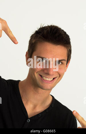 Giovane uomo sorridente e puntando verso di sé con successo Foto Stock