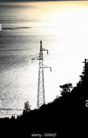 Elettricità pilone con molti cavi sul blu e giallo mare Foto Stock