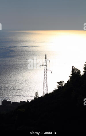 Elettricità pilone con molti cavi sul blu e giallo mare Foto Stock