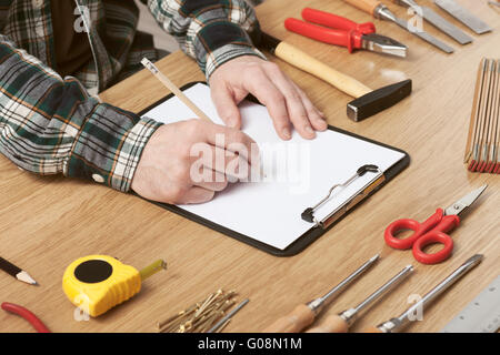 L'uomo delineando un progetto DIY su un blocco appunti con gli strumenti di lavoro tutto intorno, le mani vicino, hobby e concetto di artigianato Foto Stock