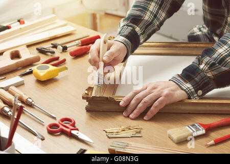 L'uomo la verniciatura di un telaio in legno mani da vicino con gli strumenti per il fai da te su di un tavolo di lavoro Foto Stock