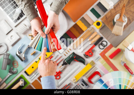 Maschio di mani tenendo i campioni e la scelta del colore giusto, strumenti di lavoro sullo sfondo vista superiore, FAI DA TE e home concetto di rinnovamento Foto Stock