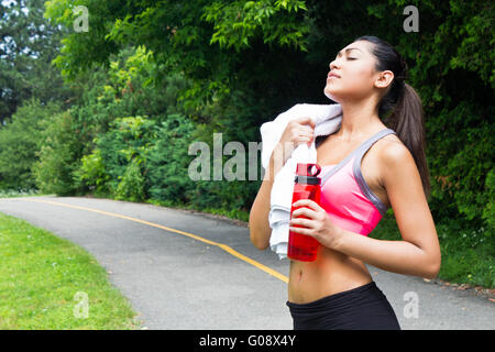 Giovane donna appoggiata con asciugamani e acqua in bottiglia dopo l'esecuzione Foto Stock