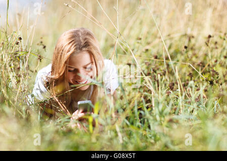 Ragazza è la scrittura di sms sul telefono giacente in erba Foto Stock