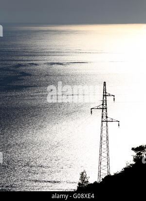 Elettricità pilone con molti cavi sul blu e giallo mare Foto Stock