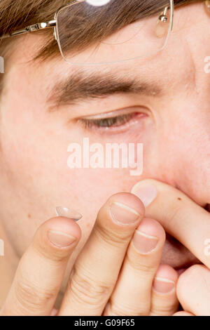 Primo piano di un uomo occhio marrone mentre inserendo un correttivo lente a contatto su un dito. Foto Stock