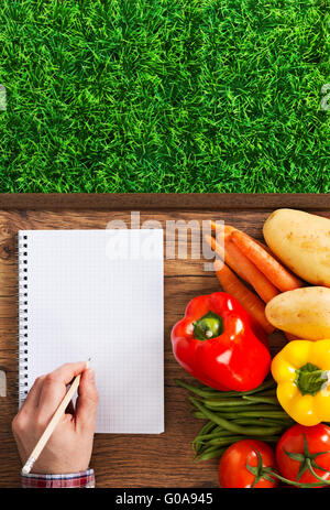 Coltivatore notebook con verdure fresche e il verde erba, maschio la scrittura a mano con una matita Foto Stock