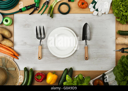 Utensili da giardinaggio e le verdure che compongono un telaio, tabella imposta al centro composta di piatto, diserbo forcella e cazzuola, vista dall'alto Foto Stock