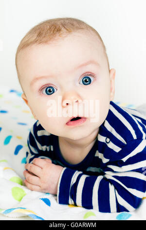 Carino bambino in abiti a strisce sdraiati su una coperta Foto Stock
