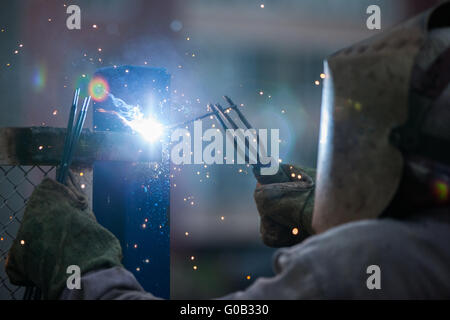 Saldatrice ad arco lavoratore nella maschera di protezione in metallo di saldatura Foto Stock