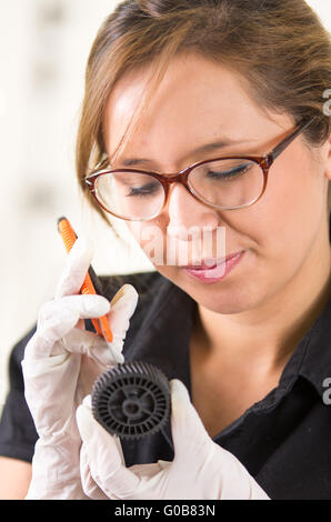 Giovane donna che indossa la maglia nera tenendo in mano le parti di toner e esaminando da vicino mentre si esegue la manutenzione, concentrato le espressioni del viso Foto Stock