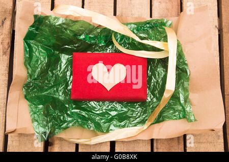 Rosso presente giacente sulla plastica di colore verde con riflessi dorati stringa di nastro intorno ad esso, come visto da sopra Foto Stock