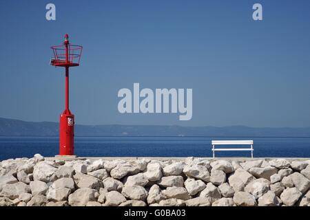 Faro rosso in porto con pietre e banco di bianco. podgora, Croazia. Foto Stock