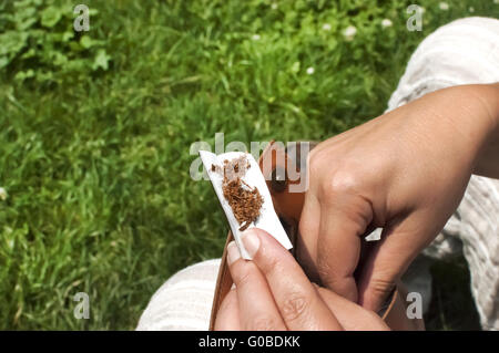 Mani femminili che mettono il tabacco sulla carta di sigaretta Foto Stock