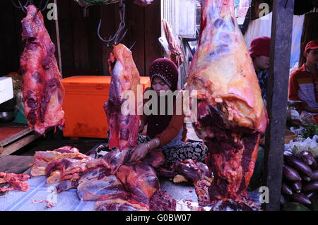 Giovane donna musulmana fornitore di carne di manzo cruda al mercato locale all'aperto, carne rossa appesa a ganci di carne, Senmonorom, Provincia di Mondulkiri, Cambogia. © Kraig Lieb Foto Stock