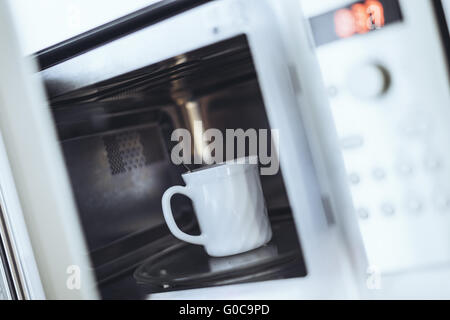 Una tazza bianca con cucchiaio in vendita nel forno a microonde ov Foto Stock