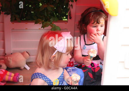 Due anno vecchia ragazza amici mangiare coni gelato insieme seduta playhouse in giardino, bambine seduti insieme, concetto di infanzia bambini Foto Stock