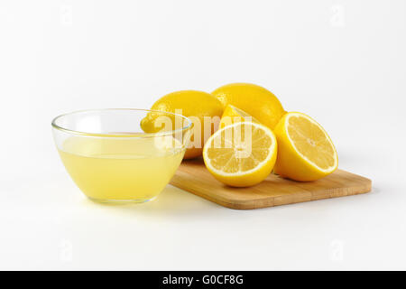 Ciotola di spremuta di succo di limone e mature di limoni sul tagliere di legno Foto Stock