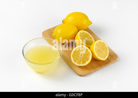 Ciotola di spremuta di succo di limone e mature di limoni sul tagliere di legno Foto Stock