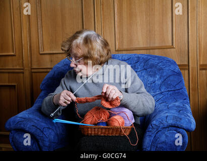 La vecchia donna si siede in una poltrona e maglieria Foto Stock