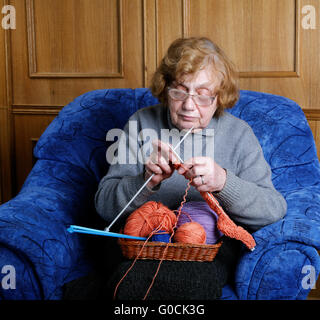 La vecchia donna si siede in una poltrona e maglieria Foto Stock