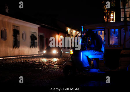 Cars driving attraverso una strada buia la notte di Antigua in una città negli altipiani centrali del Guatemala famoso per il suo ben conservato Barocco spagnolo-influenzato architettura e un Sito Patrimonio Mondiale dell'UNESCO. Foto Stock