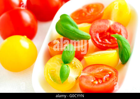 Il giallo e il rosso dei pomodori ciliegia nella piastra sulla tovaglia bianca close up Foto Stock