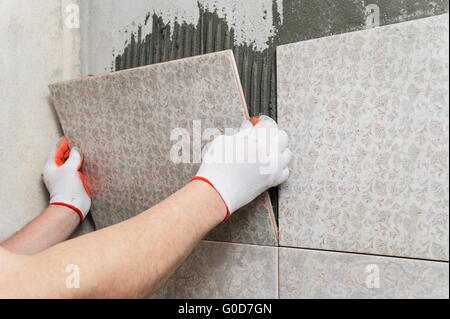 La posa di piastrelle in ceramica. installatore mette piastrella adesivo sulla parete. Foto Stock