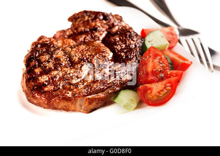 Bistecca alla griglia e verdura sulla piastra bianca con utensili da cucina Foto Stock