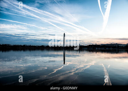 Washington DC -- linea Contrails il cielo sopra Washington DC su una mattina tranquilla e sono riflessi sull'acqua ancora del bacino di marea. Il Monumento di Washington è al centro del telaio. Foto Stock