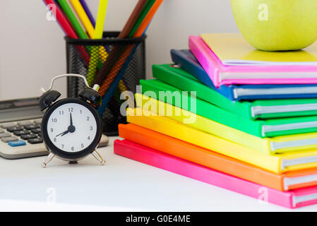 Nero orologio sveglia e colorato i libri in pila Foto Stock