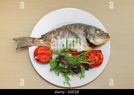 Grigliata di pesce dorado con pomodorini, rucola e basilico su piastra bianca Foto Stock