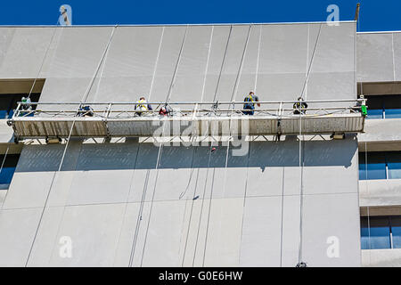 Un Ponteggio sospeso piattaforma alto sopra la strada a un alto edificio con gli uomini al lavoro per pulire l'edificio Foto Stock