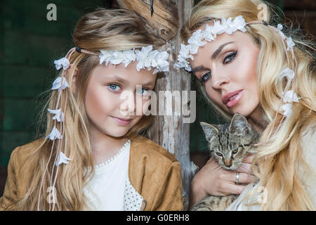 Una bella donna bionda con una bambina snuggling sul selvaggio west in costumi bianchi con un gatto sulle mani Foto Stock