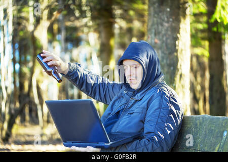 Uomo con bottiglia di birra e il PC nel parco su un banco di lavoro Foto Stock