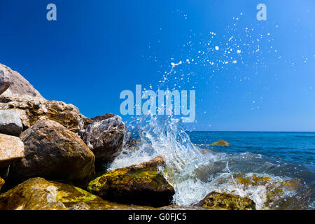 Le onde di colpire le rocce su una spiaggia tropicale formando una forma iniziale. La Grecia Foto Stock