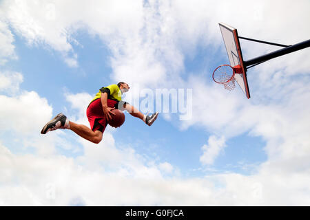 Giovane uomo di salto e facendo un fantastico Slam Dunk giocando streetball Foto Stock