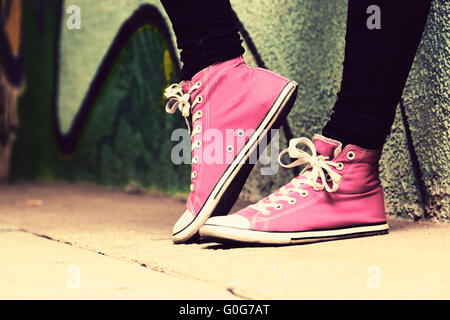 Close up di rosa sneakers indossata da un adolescente. Grunge muro di graffiti Foto Stock