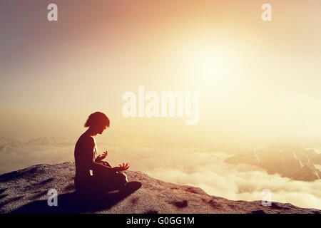 Uomo asiatico medita in posizione di yoga in alta montagna sopra le nuvole al tramonto. Concetto unico di meditazione Foto Stock